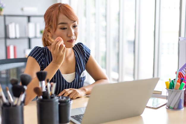 Artista de maquillaje influyente femenina asiática hablando de maquillaje en la computadora portátil en casa.