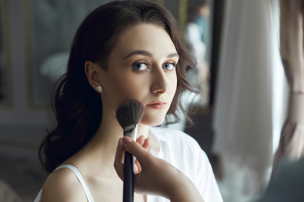 Artista de maquillaje maquilla a una mujer hermosa por la mañana.