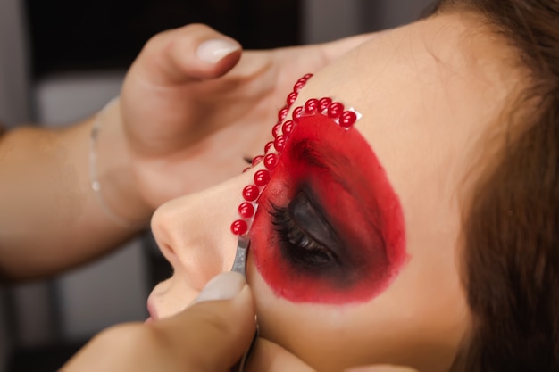 Artista de maquillaje pegando lentejuelas en el borde de los ojos de una niña