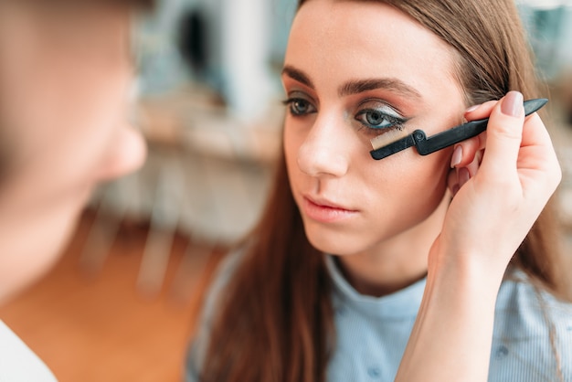 Artista de maquillaje con pincel en mano trabaja con pestañas de mujer en estudio de belleza