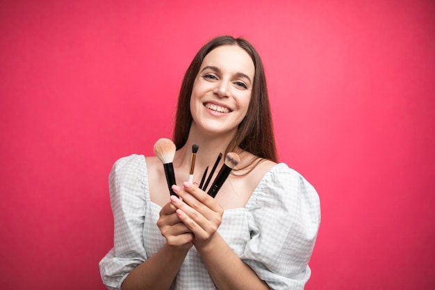 Artista de maquillaje con pinceles en la mano sobre un fondo rosa