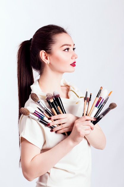 Artista de maquillaje con pinceles en mano sobre una pared blanca