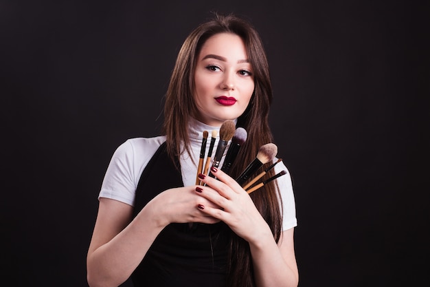 Artista de maquillaje con pinceles en mano sobre una pared negra