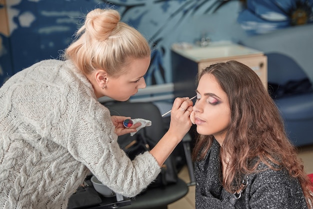 Artista de maquillaje pone sombras en los párpados de una mujer joven