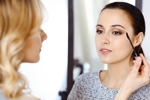 Artista de maquillaje profesional trabajando con una hermosa joven. Estilo nupcial, fashion o nude. Concepto de belleza.