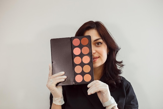 Foto artista de maquillaje que muestra la paleta de sombras de ojos paleta de colores nude fondo blanco.