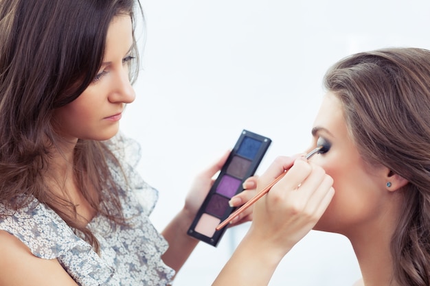 Artista de maquillaje sosteniendo la paleta de sombras de ojos y aplicando maquillaje, enfoque selectivo en el ojo del modelo
