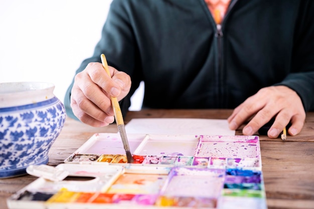 Artista masculino asiático pinta com pincel e paleta de aquarela