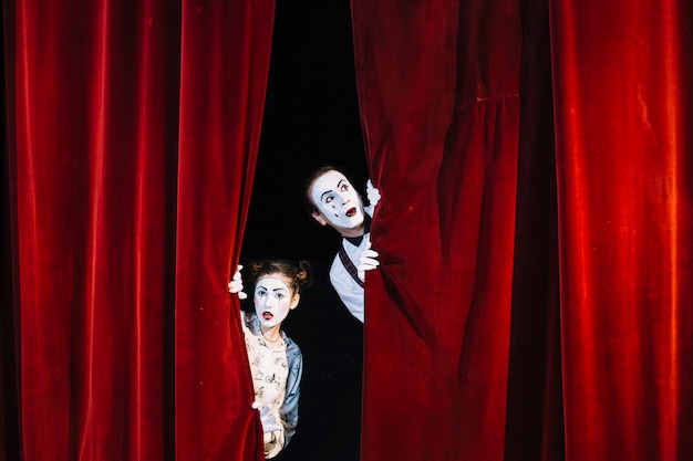 Artista masculino y femenino del mime que mira a escondidas de la cortina roja