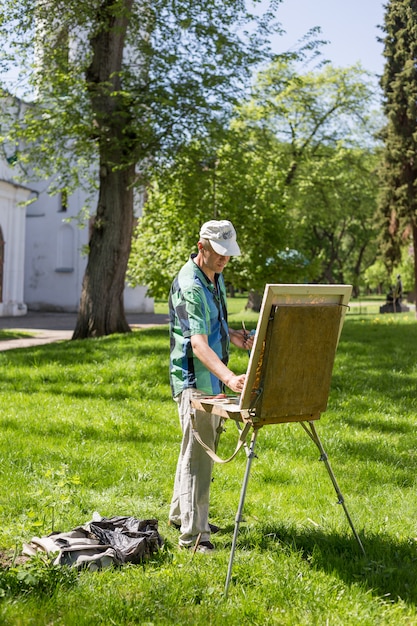 Artista masculino trabalhando ao ar livre no parque ou jardim em um cavalete e pintura de cavalete