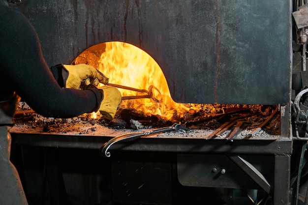 Artista de metal femenino elige una pieza de trabajo de un horno de herrería ardiente tradicional con pinzas