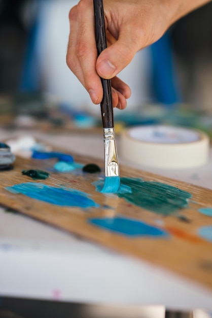 Artista mezcla pinturas con un pincel en una paleta.