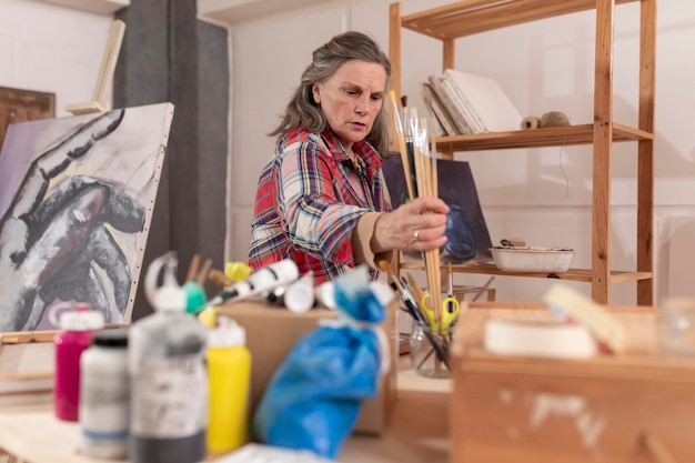 Artista mujer madura preparando pinceles antes del trabajo