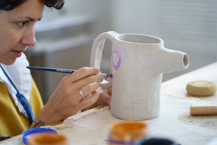 Foto artista mujer mantenga pincel creando adornos en jarra de arcilla en el lugar de trabajo de ceramista de estudio de alfarería