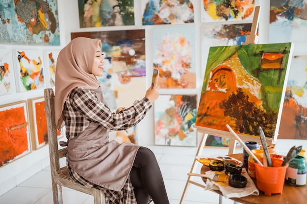Foto artista musulmana tomando una foto de su propia pintura usando un teléfono inteligente
