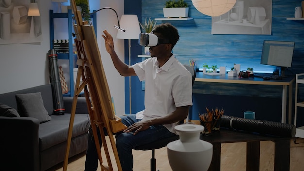 Artista negro usando óculos vr para inspiração de desenho virtual no estúdio de oficina. Homem afro-americano criando conceito de obra-prima com tecnologia de vaso, tela branca e fone de ouvido