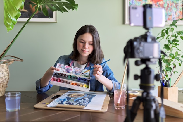 Artista niña pintando con acuarelas y haciendo videos para el blog de su canal. Niña mostrando lo que dibuja y enseñando a sus seguidores, niños y adolescentes. Formación, educación, dirección de arte