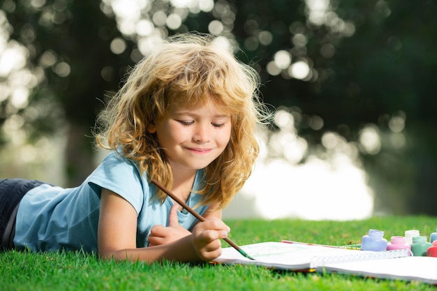 Artista niños retrato de un niño feliz sonriente disfrutando del arte y el dibujo artesanal en el patio trasero o en el parque de primavera...
