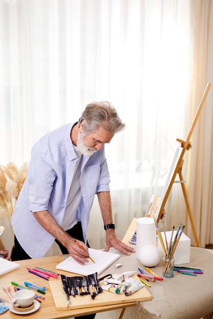 Artista de pelo gris concentrado en el trabajo mirando hacia abajo en la hoja, sosteniendo un lápiz en las manos