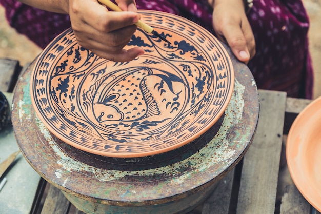 Artista pintando patrón de pescado en cerámica artesanal