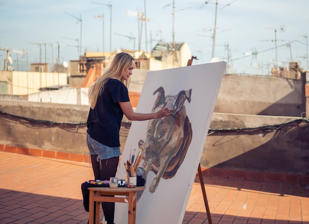 Artista de pintura joven dibujando en el techo de su casa. Cuadro de bulldog sobre lienzo grande. Arte al aire libre