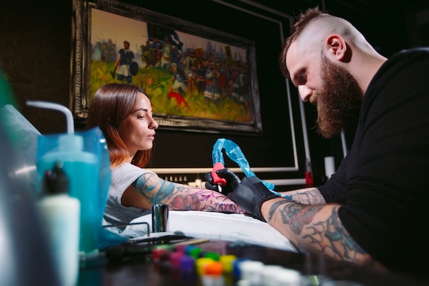 El artista profesional del tatuaje hace un tatuaje en la mano de una niña.