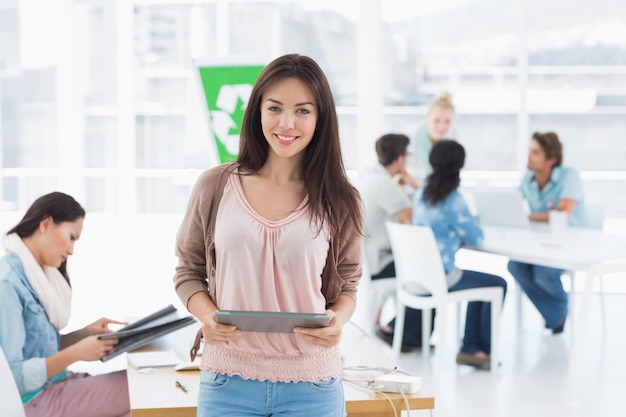 Artista segurando comprimido digital com colegas em segundo plano no escritório