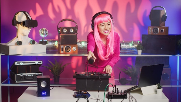 Artista sonriente parado en la mesa de dj disfrutando de mezclar sonidos estéreo con electrónica, divirtiéndose en el club por la noche. Intérprete asiático disfrutando de tocar música con equipos de audio profesionales