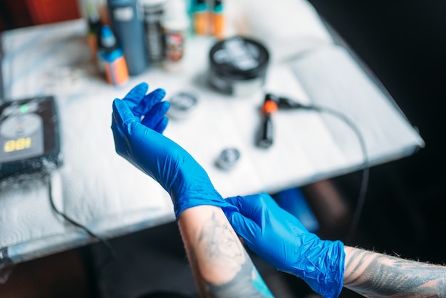 Artista del tatuaje femenino manos en guantes estériles azules, herramientas de trabajo profesional. tatuaje en el salón