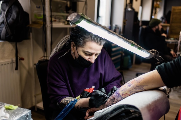 Un artista del tatuaje hace un tatuaje en un salón.