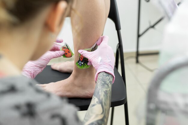 Artista del tatuaje pone un dibujo de una mariquita en la pierna de una mujer joven el proceso de creación