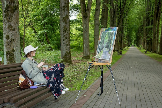 la artista tiene un refrigerio en el parque mirando su cuadro que acaba de pintar