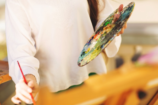 Artista trigueno joven de la mujer que sostiene en manos un cepillo y una paleta.