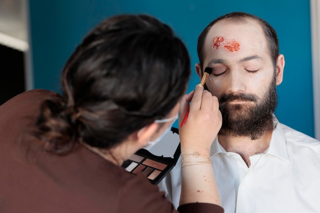 Artista usando efeitos de maquiagem para criar fantasia de zumbi e aparência de cadáver dramático assustador. Homem parecendo morto e infectado depois de ter cicatrizes sangrentas e rosto de monstro, design assustador.