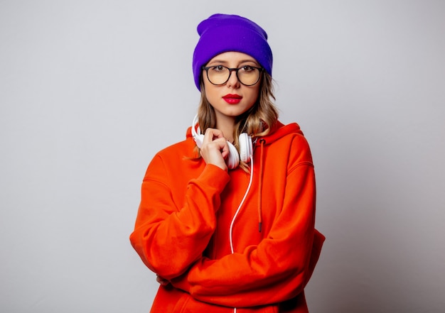 Artmädchen im orange Hoodie und im purpurroten Hut mit Kopfhörern