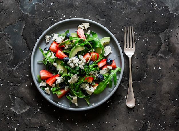 Arugula-Erdbeer-Gorgonzola-Avocado-Salat auf Draufsicht eines dunklen Hintergrundes