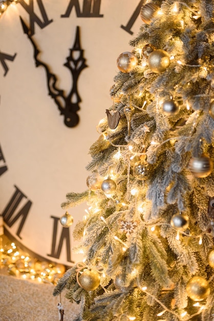 Árvore de natal com brinquedos dourados garland na foto vertical grande relógio em segundo plano mostra meia-noite