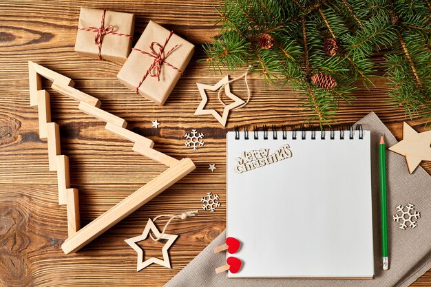 Árvore de Natal de madeira com velas dentro de caixas de presente ramos de pinheiro e estrelas com caderno em branco