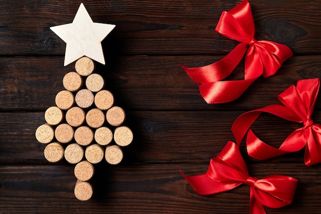 Árvore de natal de rolhas de vinho com uma estrela no topo em um fundo de madeira com laços vermelhos