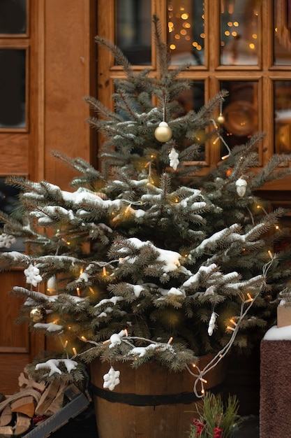 Árvore de natal decorada com uma guirlanda com flocos de neve de bolas de luz sob uma janela na rua