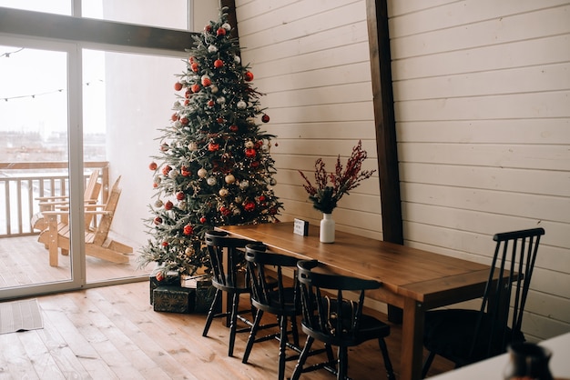 Árvore de natal decorada em uma mesa de madeira em uma casa de campo no estilo de um chalé com terraço e uma grande janela.