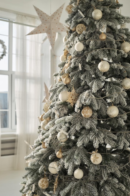 Árvore de Natal nevada artificial, luxuriante, decorada com velas de bolas douradas brancas, luzes de guirlanda fechadas no interior branco