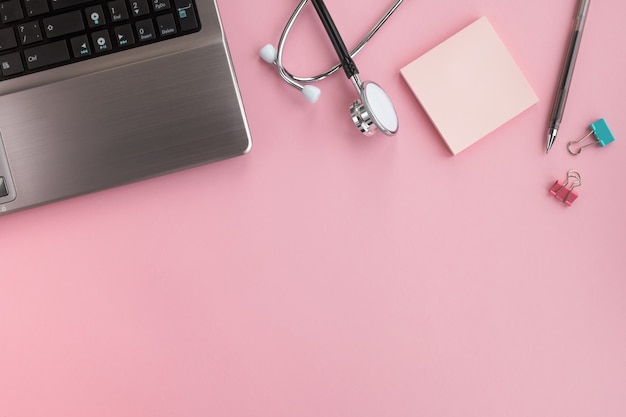 Arzt am Arbeitsplatz. Medizinisches Stethoskop, Laptop und Stift auf rosa Schreibtisch