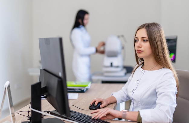 Arzt arbeitet am Computer im Klinikbüro. Sanitäter im weißen Kittel sitzt am Tisch. Modernes Interieur im Krankenhaus.