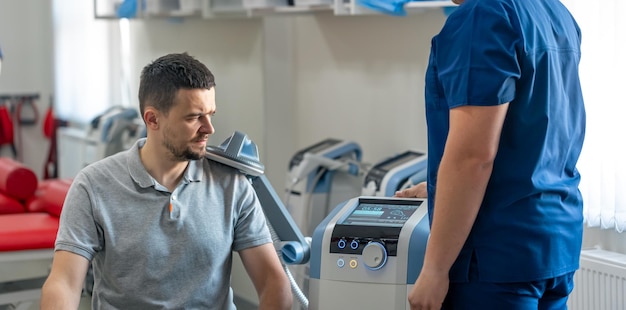 Arzt benutzt eine Maschine, um die Schultern des Patienten zu behandeln