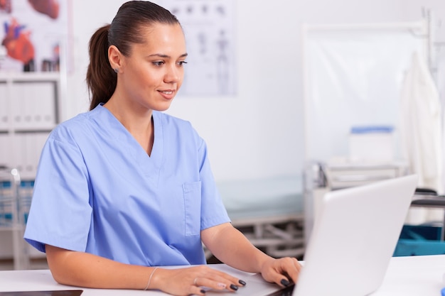 Arzt, der am Laptop sitzt und blaue Uniform trägt. Arzt im Gesundheitswesen mit Computer in moderner Klinik mit Blick auf Monitor, Medizin, Beruf, Peelings.