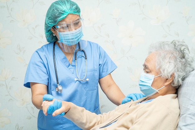 Arzt, der asiatische ältere Patientin überprüft, die eine Gesichtsmaske im Krankenhaus trägt, um Covid-19 Coronavirus zu schützen.