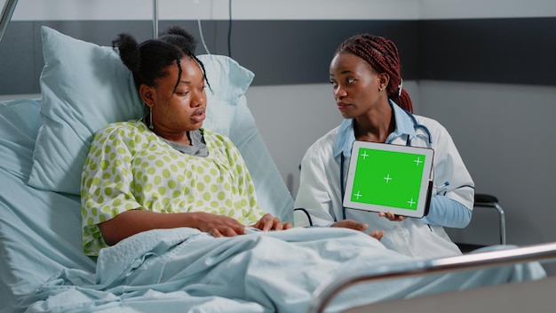 Arzt, der ein digitales Tablet mit horizontalem grünem Bildschirm hält und dem Patienten die Technologie zeigt. Sanitäter und Person betrachten isolierte Mockup-Vorlage und Hintergrund auf dem Chroma-Key-Display