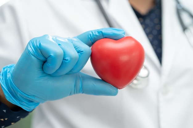 Arzt, der ein rotes Herz in der Krankenstation hält, gesundes, starkes medizinisches Konzept