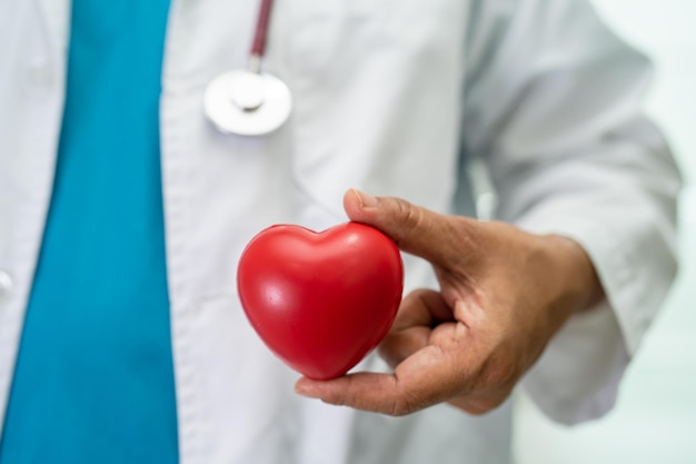 Arzt, der ein rotes Herz in der Krankenstation hält, gesundes, starkes medizinisches Konzept